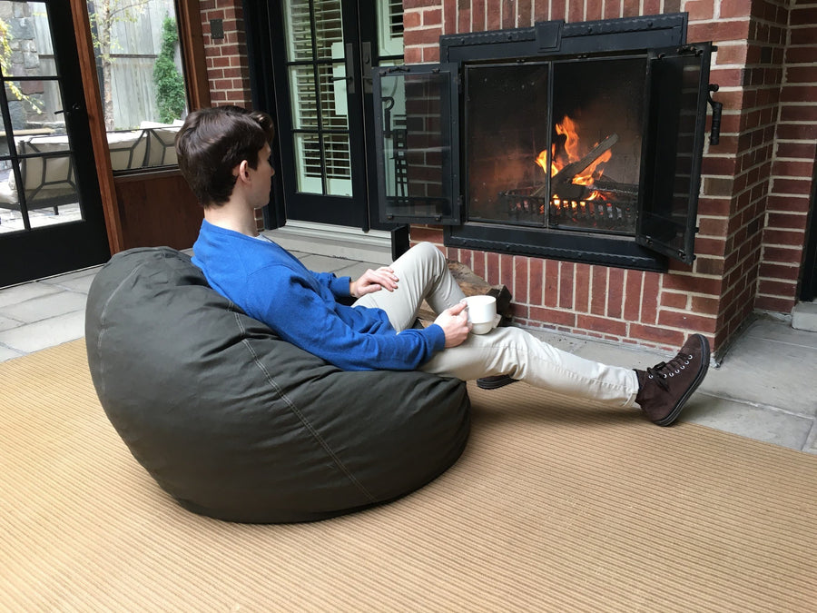 Person relaxing on ComfyBean adult bean bag lounger beside a fireplace in a cozy living room