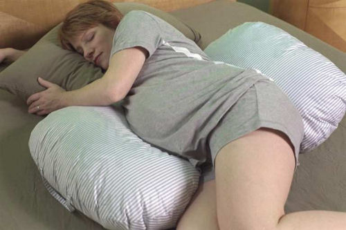Pregnant woman sleeping with U-shaped maternity pregnancy pillow providing belly, back and hip support for comfortable side sleep