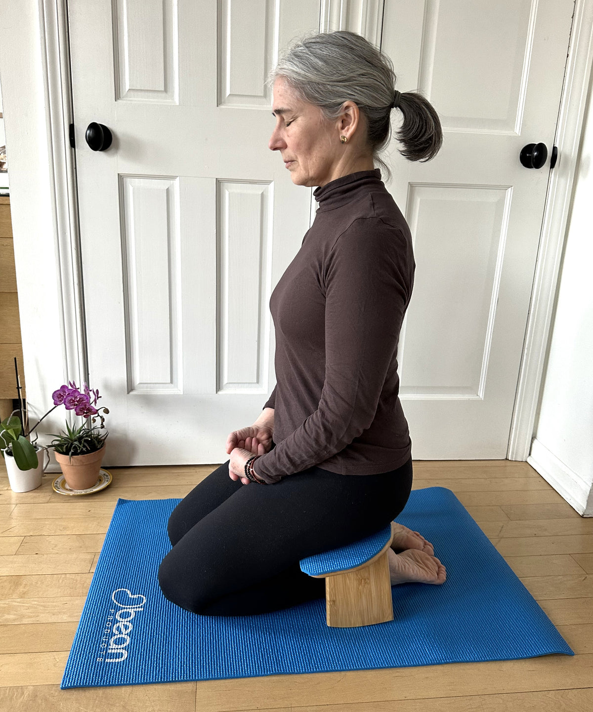 Woman kneeling on bamboo meditation bench practicing meditation indoors