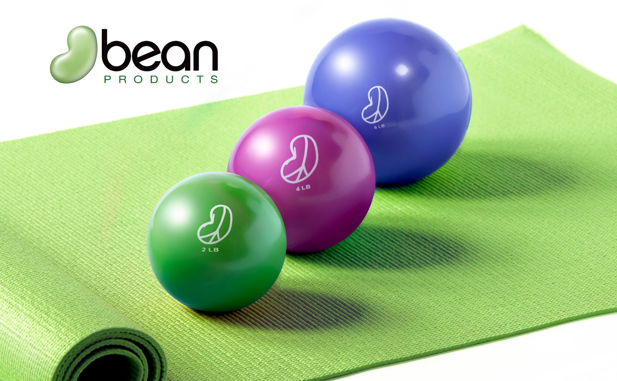 Three colorful soft weighted vinyl covered sand and iron filled exercise balls on a green mat with 'bean products' branding.