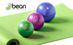 Three colorful soft weighted vinyl covered sand and iron filled exercise balls on a green mat with 'bean products' branding.