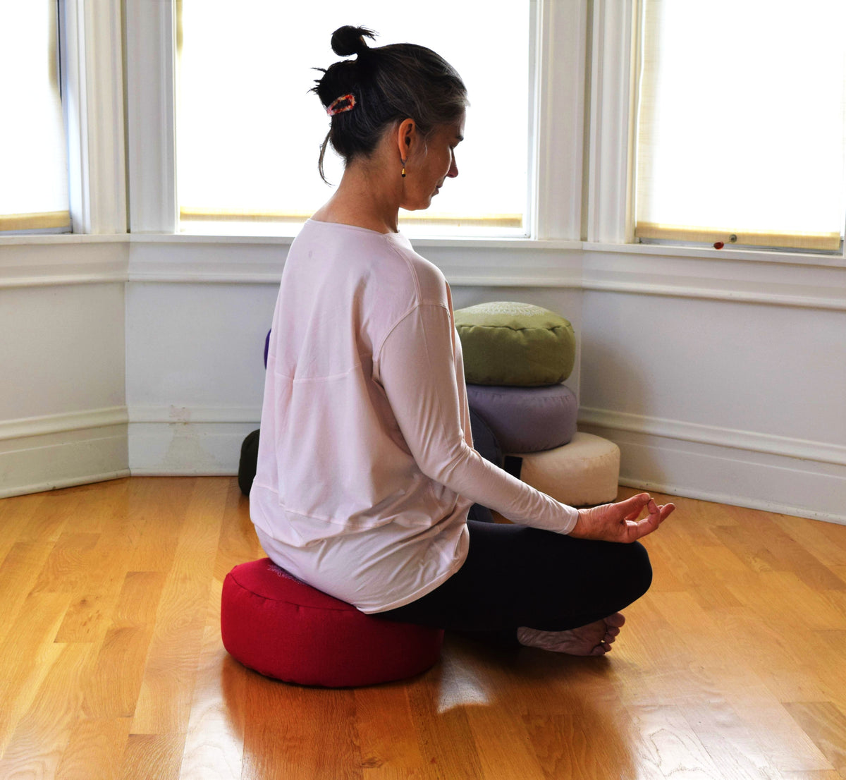 Woman meditating on round zafu cushion in bright room, cross-legged yoga posture