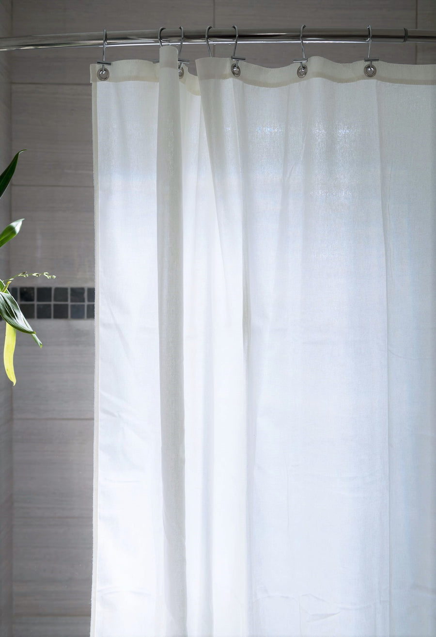 White organic cotton shower curtain hanging in bathroom with metal hooks