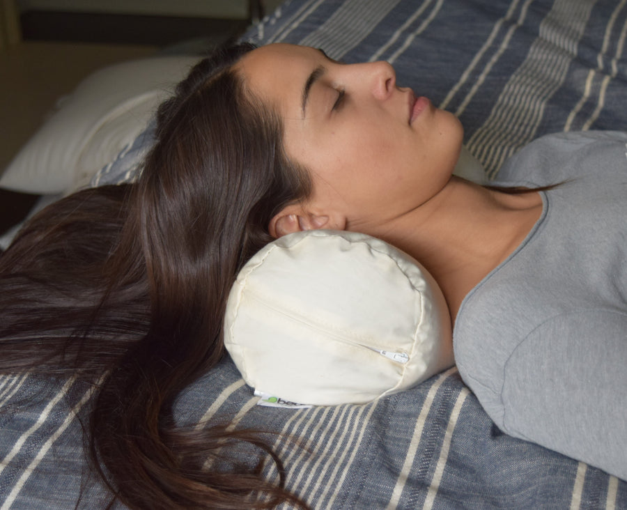 Woman resting on organic buckwheat neck roll pillow for cervical support in bed