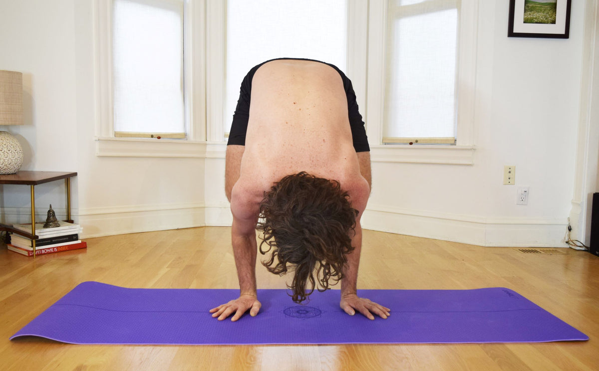 Dark purple yoga mat used for forward fold pose showing full body alignment support