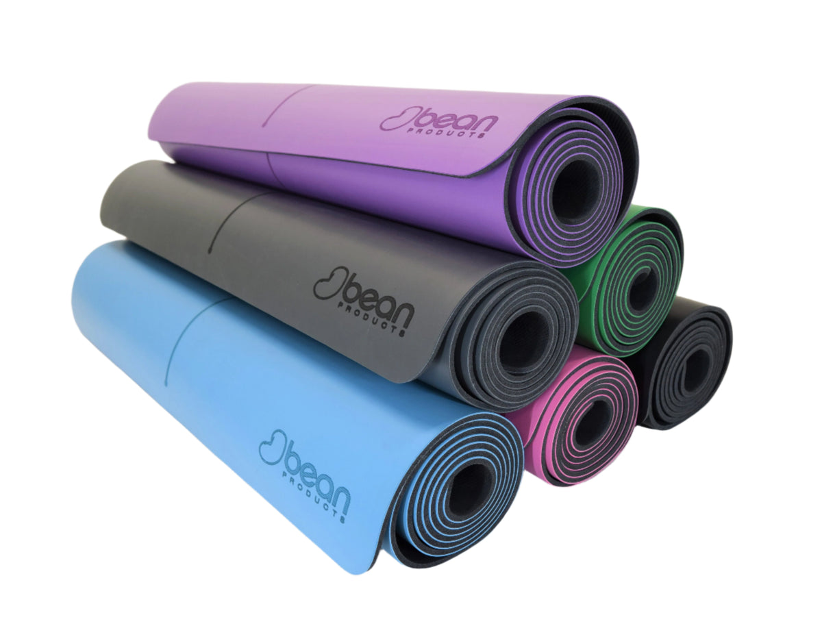 Stack of non-slip yoga mats in multiple colors including purple, blue, green, gray, and pink made from natural rubber PU