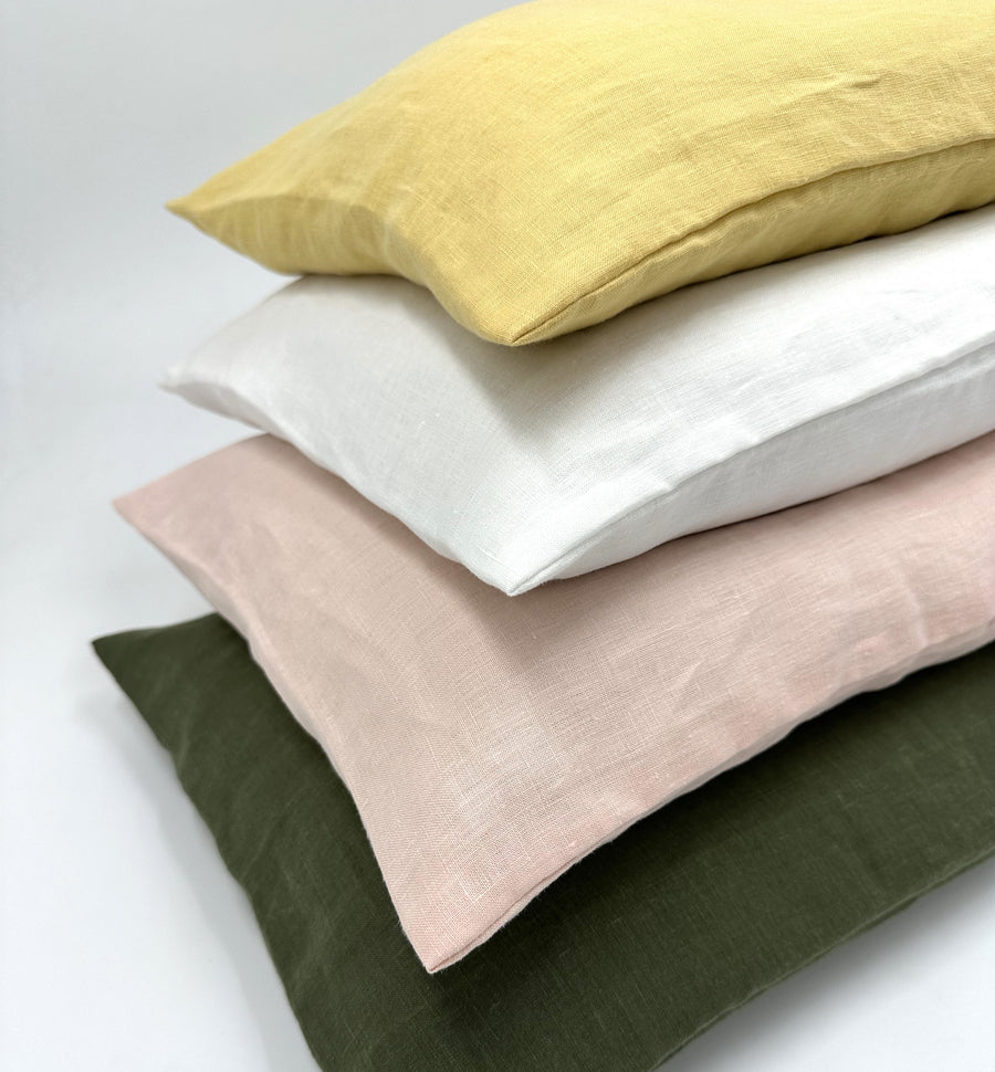 Stack of hemp pillowcases in mustard, white, blush pink, and olive green showing soft breathable natural fabric